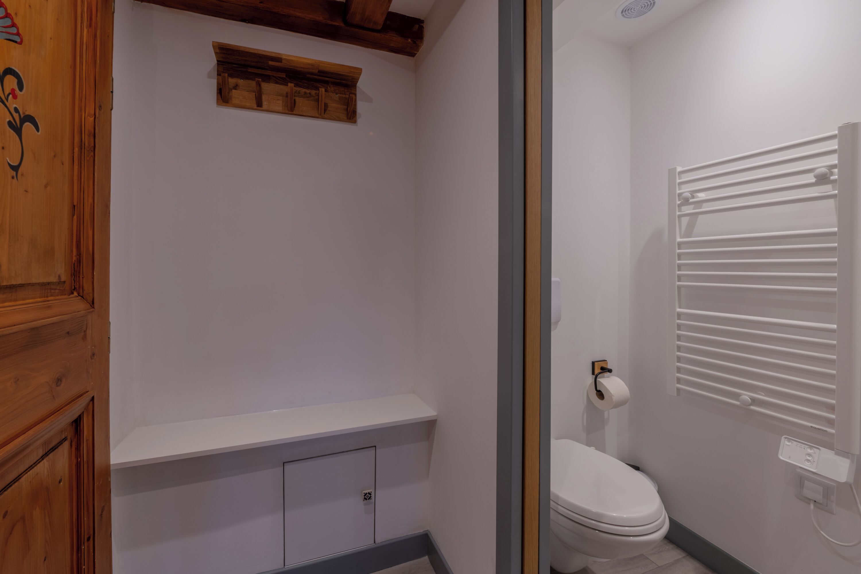 A bathroom with a white toilet, a towel rack, and a wooden shelf.