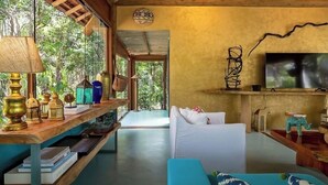 Ein Zimmer mit Holzboden, einem weißen Sofa, einem blauen Sessel, einem an der Wand befestigten Fernseher und einem Regal mit Dekoration.