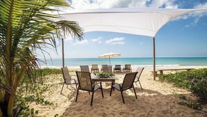 Ein Tisch mit Stühlen am Strand unter einer Markise mit Blick auf das Meer.