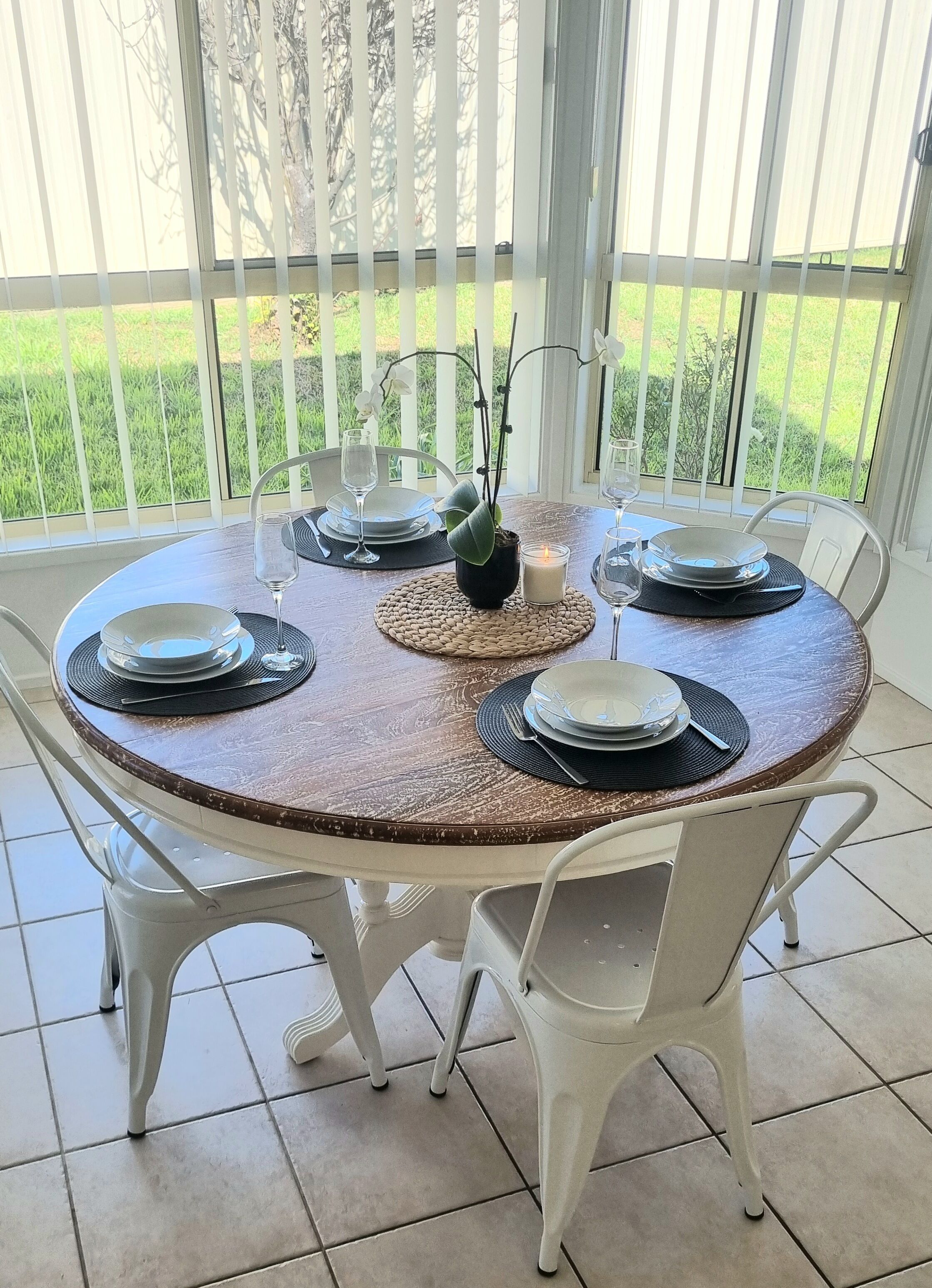 Une table ronde entourée de chaises blanches, mise avec des assiettes, des verres et une bougie.