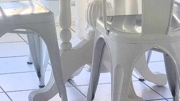 A white dining table with chairs, a potted plant, and a window with vertical blinds. - Glenmore Cottage (Glenmore Park)