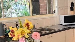 A kitchen with a wooden cutting board, a loaf of bread, a jar of jam, a cup, and a vase of flowers. - Glenmore Cottage (Glenmore Park)