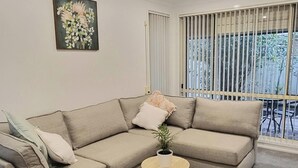 A modern living room with a beige sectional sofa, a small round side table, and a single potted plant. - Glenmore Cottage (Glenmore Park)