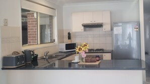 A modern kitchen with a built-in microwave, toaster, sink, and stainless steel refrigerator. - Glenmore Cottage (Glenmore Park)