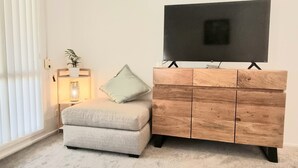 A living room with a grey sofa, a wooden TV stand, a TV, a floor lamp, and a potted plant. - Glenmore Cottage (Glenmore Park)