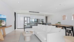 A modern living room with a white sectional sofa, a round coffee table, and a dining area with a wooden table and chairs. - Relax in luxury, a short walk to the beach (Gold Coast)