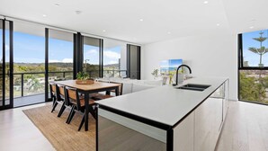A modern kitchen with a large island, a dining area with a table and chairs, and large windows offering a view of the city. - Relax in luxury, a short walk to the beach (Gold Coast)