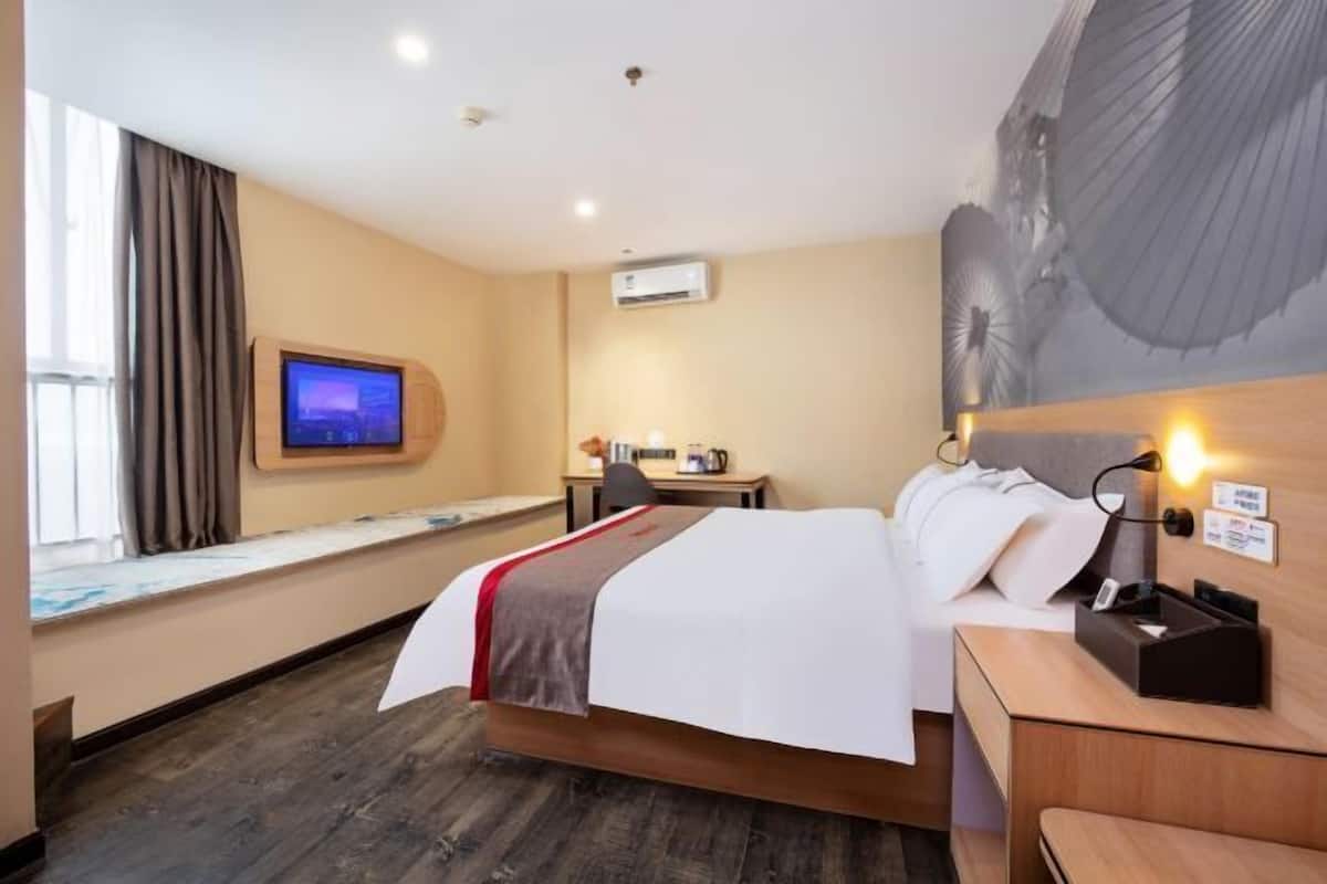 A hotel room with a bed, a desk, a television, and a window with curtains.