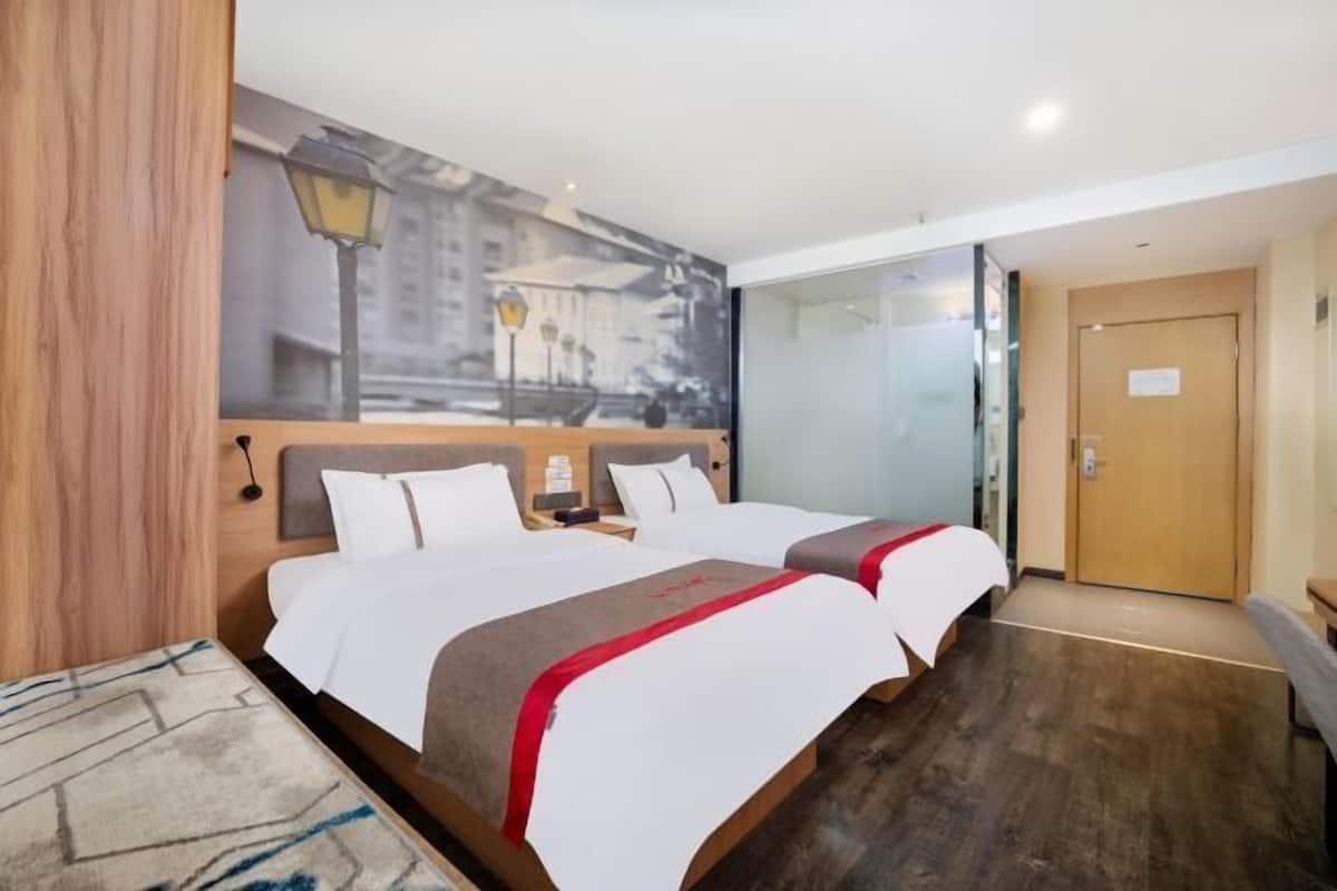 A hotel room with two beds, a cityscape mural, a wooden headboard, a nightstand, and a door.