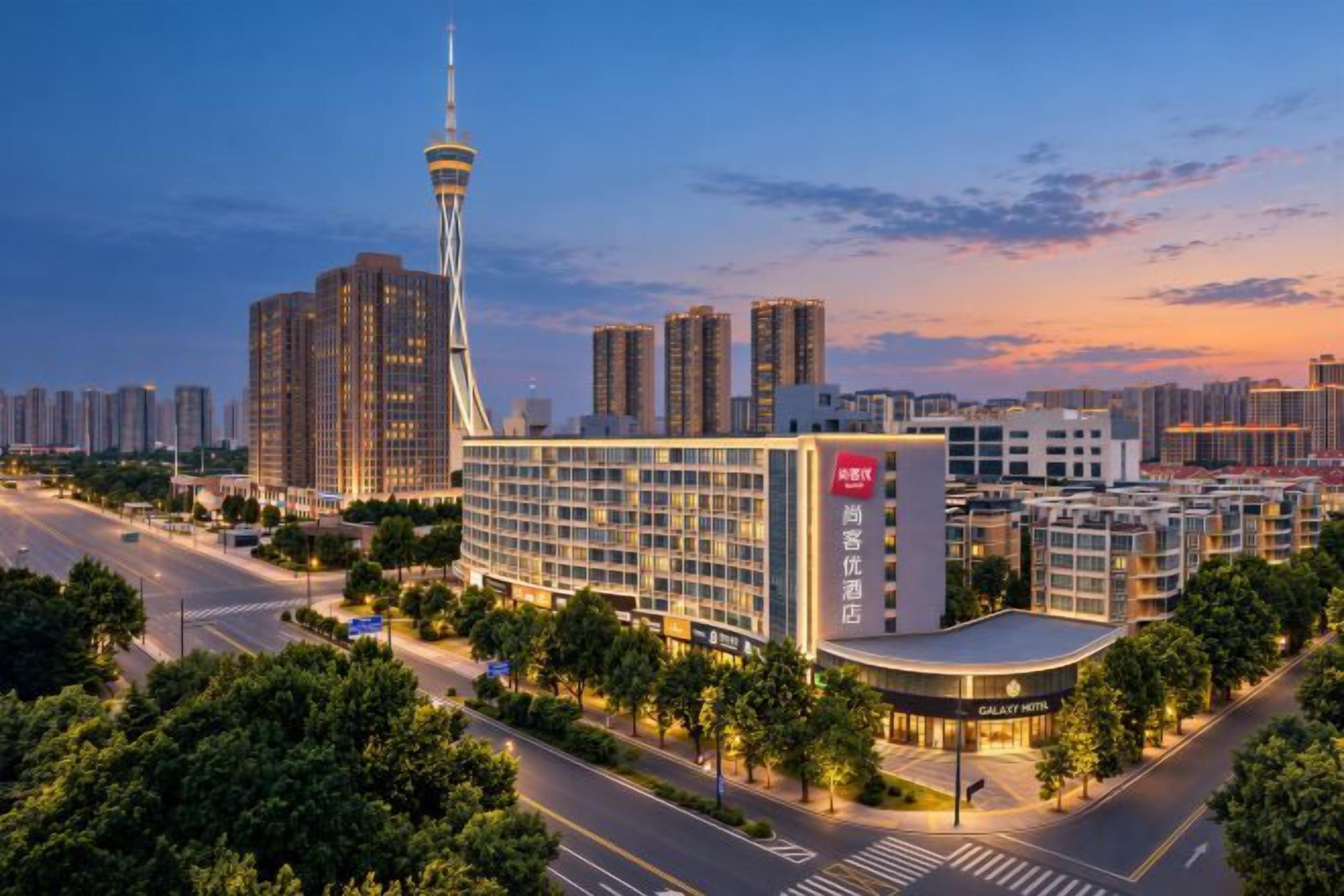 A modern hotel with a prominent tower, surrounded by high-rise buildings and a well-lit street at dusk.