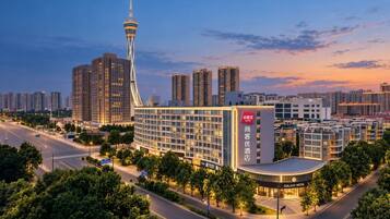 A modern hotel with a prominent tower, surrounded by high-rise buildings and a well-lit street at dusk.