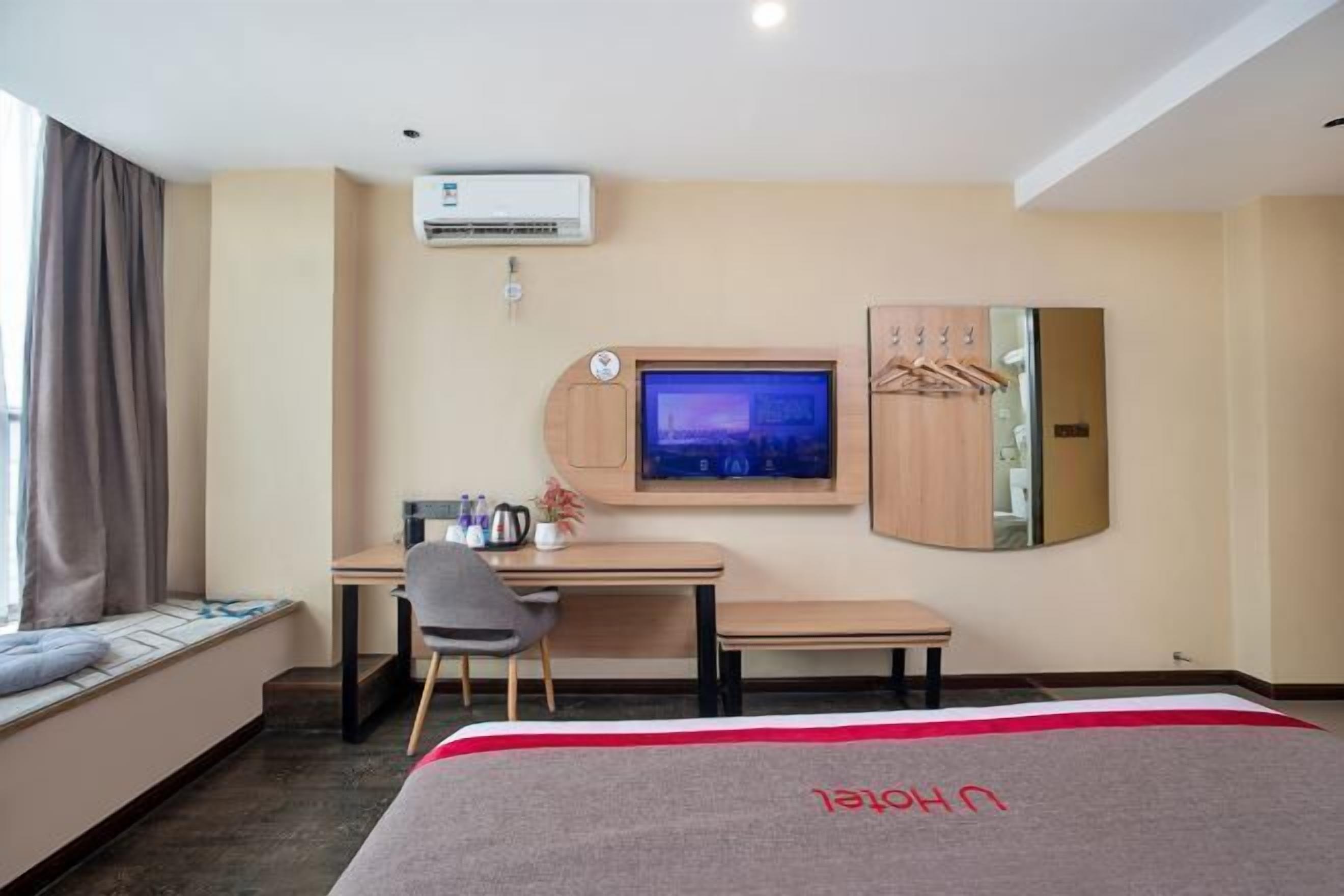 A hotel room with a bed, a desk, a chair, a TV, an air conditioner, and a wardrobe.