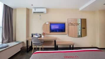 A hotel room with a bed, a desk, a chair, a TV, an air conditioner, and a wardrobe.