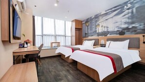 Quarto de hotel com duas camas, uma escrivaninha e uma cadeira. Há uma janela grande e um quadro na parede.