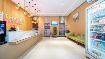 Zona de recepción de un hotel con mostrador de recepción, máquina expendedora y área de estar con un sofá.