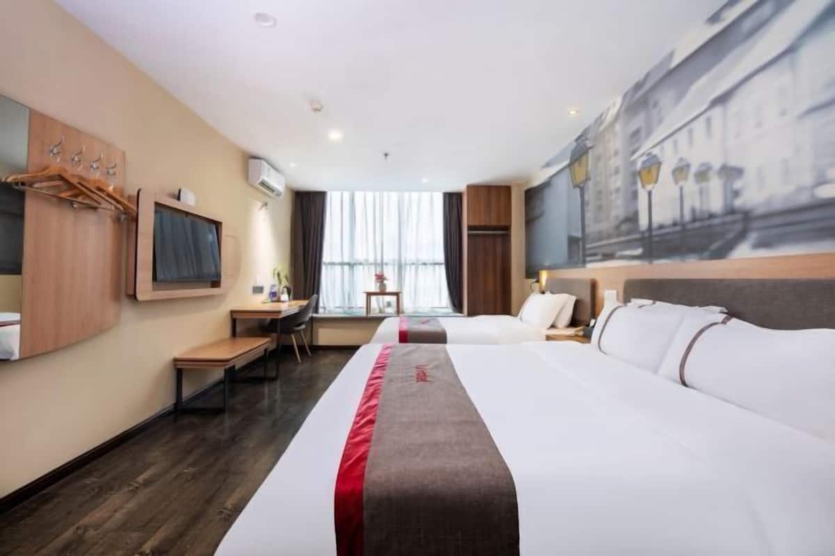 A hotel room with a large bed, a desk, a chair, a TV, and a window with curtains.