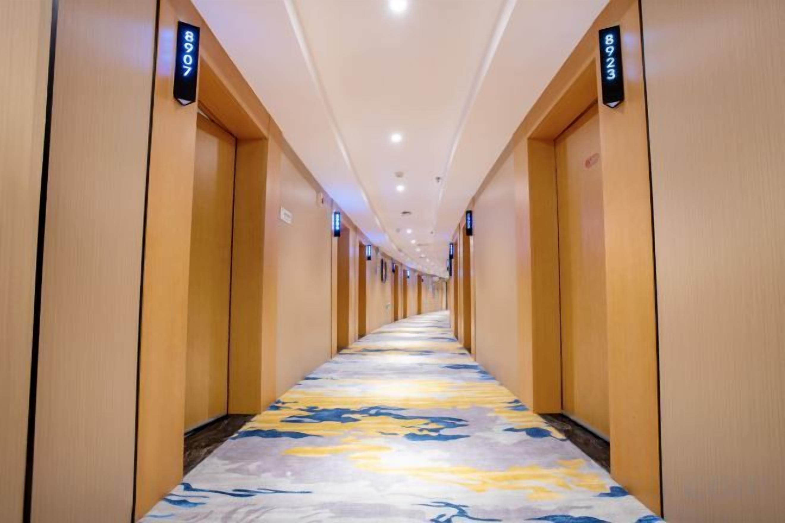 A hotel corridor with doors on both sides, a carpeted floor, and overhead lighting.