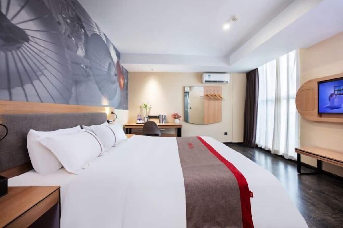A hotel room with a large bed, a desk, a chair, a TV, and a large window with curtains.