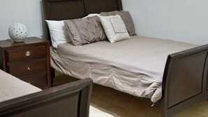 Una cama bien hecha con un cabecero marrón, una mesita de noche de madera con una lámpara decorativa y un conjunto de cajones.