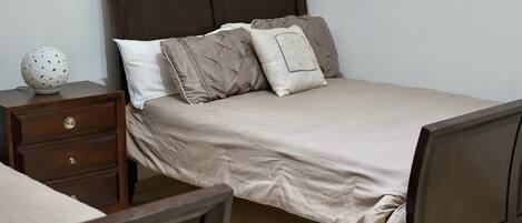 Una cama bien hecha con un cabecero marrón, una mesita de noche de madera con una lámpara decorativa y un conjunto de cajones.
