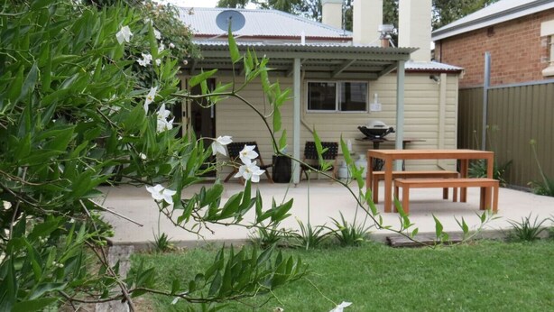 A backyard with a wooden bench, a barbecue grill, and a house with a satellite dish. - Stylish country cottage in central Orange (Orange)