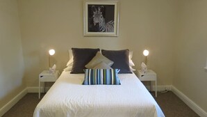 A neatly arranged bedroom with a large bed, two bedside tables, and a zebra artwork on the wall. - Stylish country cottage in central Orange (Orange)