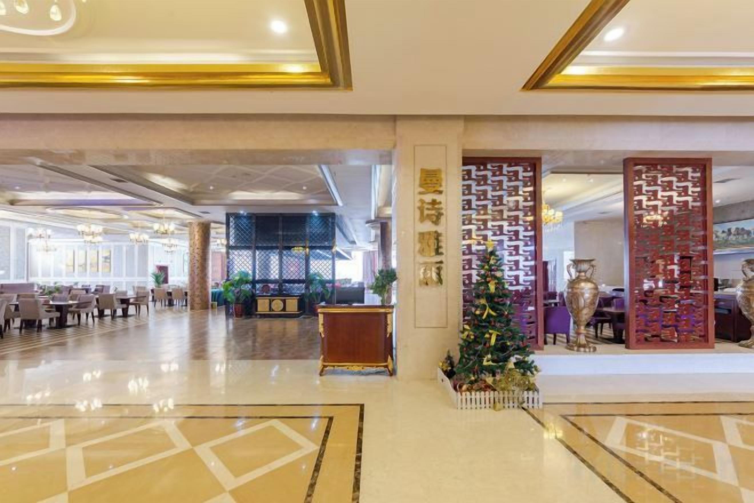 A hotel lobby with a large seating area, a reception desk, and a decorative wall with a Christmas tree.