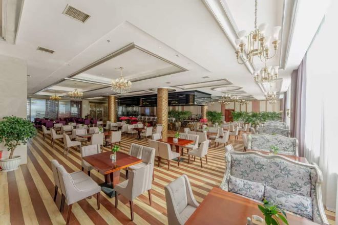 Un vestíbulo de hotel espacioso con varias zonas de estar, incluidas mesas y sillas, y una barra de bar al fondo.
