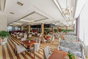 Un hall d’hôtel spacieux, doté de plusieurs espaces de détente, notamment des tables et des chaises, et d’un bar situé au fond de la pièce.