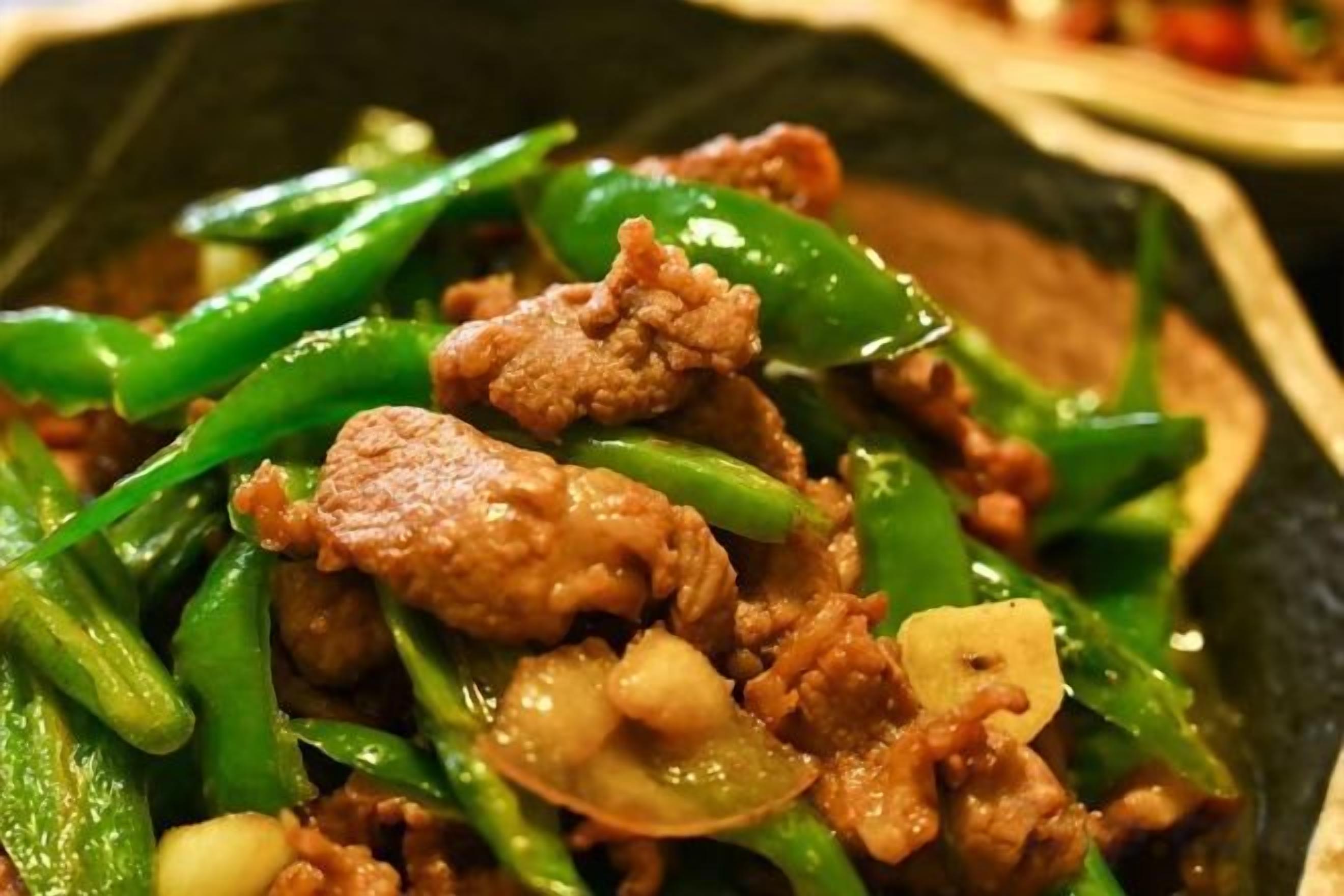 A close-up of a stir-fried dish with meat and green vegetables.