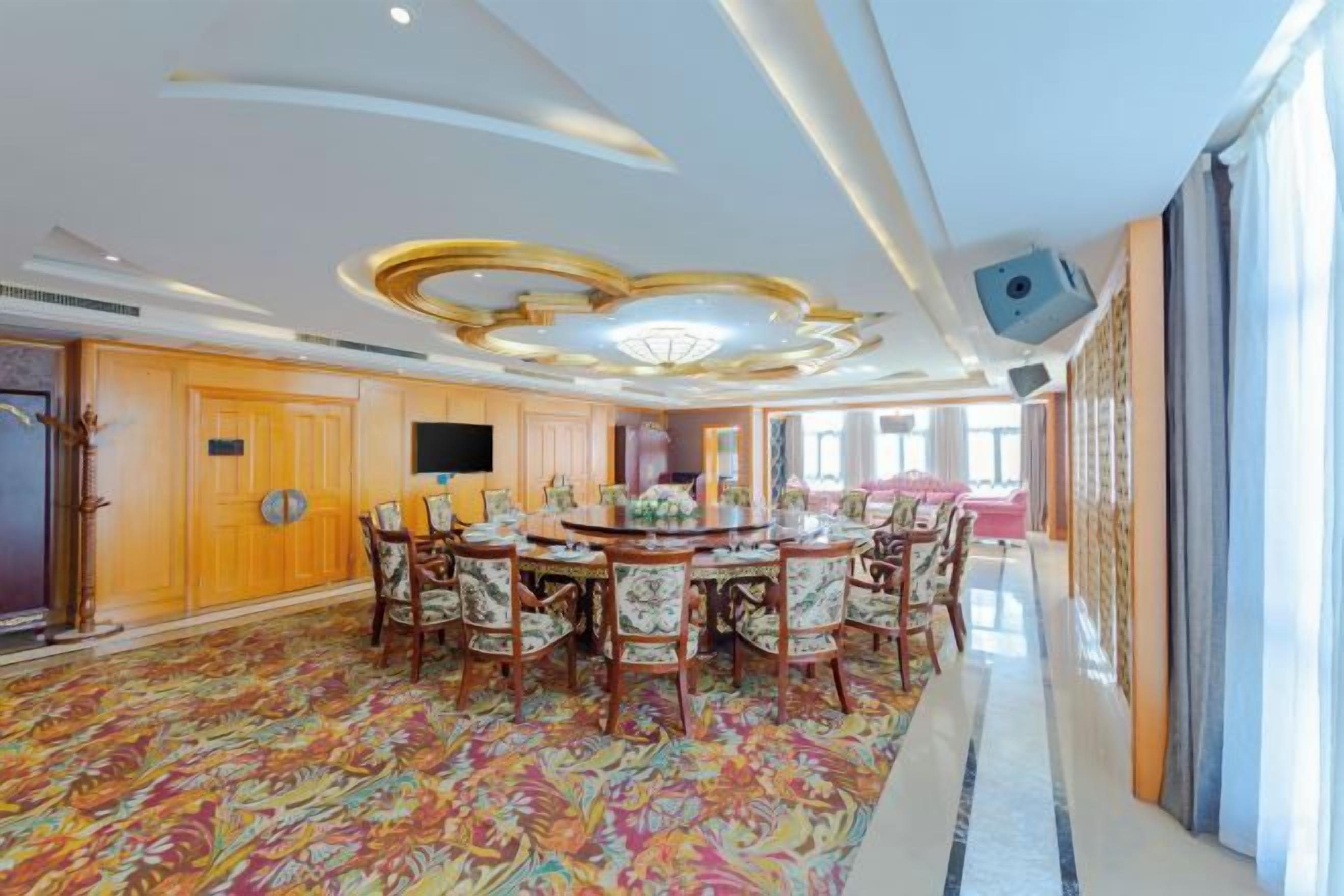 A spacious dining area with a round table and chairs, a television, and a patterned carpet.