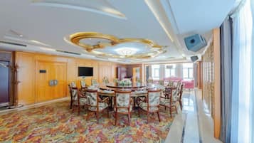 A spacious dining area with a round table and chairs, a television, and a patterned carpet.