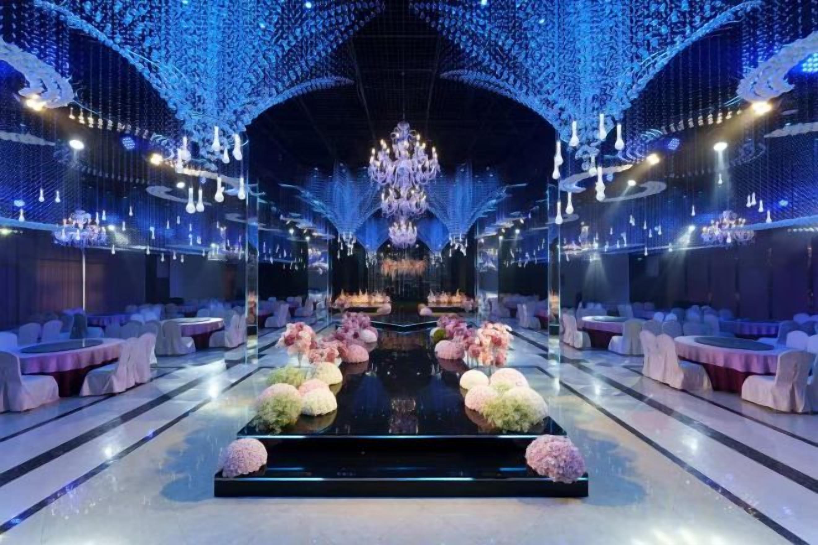 Un amplio salón con piso reflectante, un arreglo floral central y una araña.