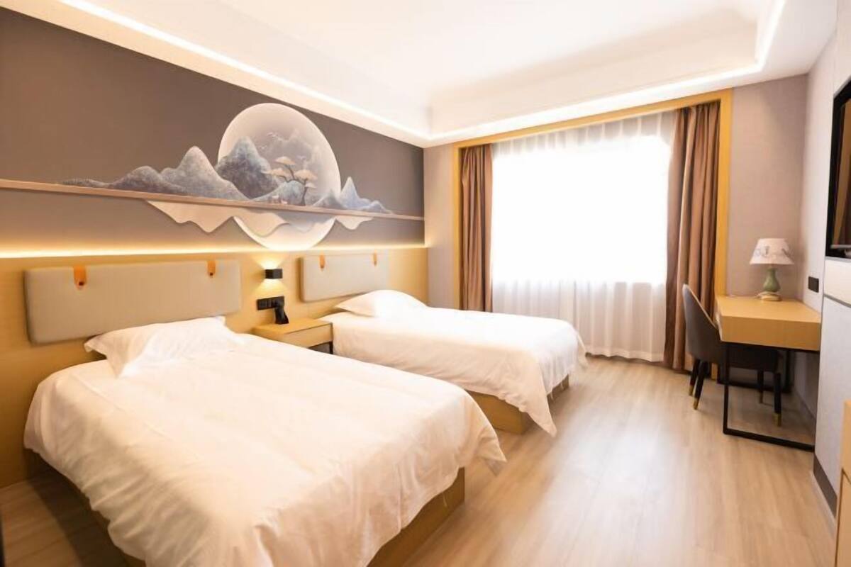 Une chambre d’hôtel avec deux lits, un bureau, une chaise, une lampe et un tableau au mur.