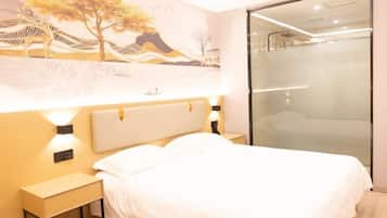 Una habitación de hotel moderna con una cama grande, una mesita de noche, un panel de control en la pared y un box de ducha de vidrio.