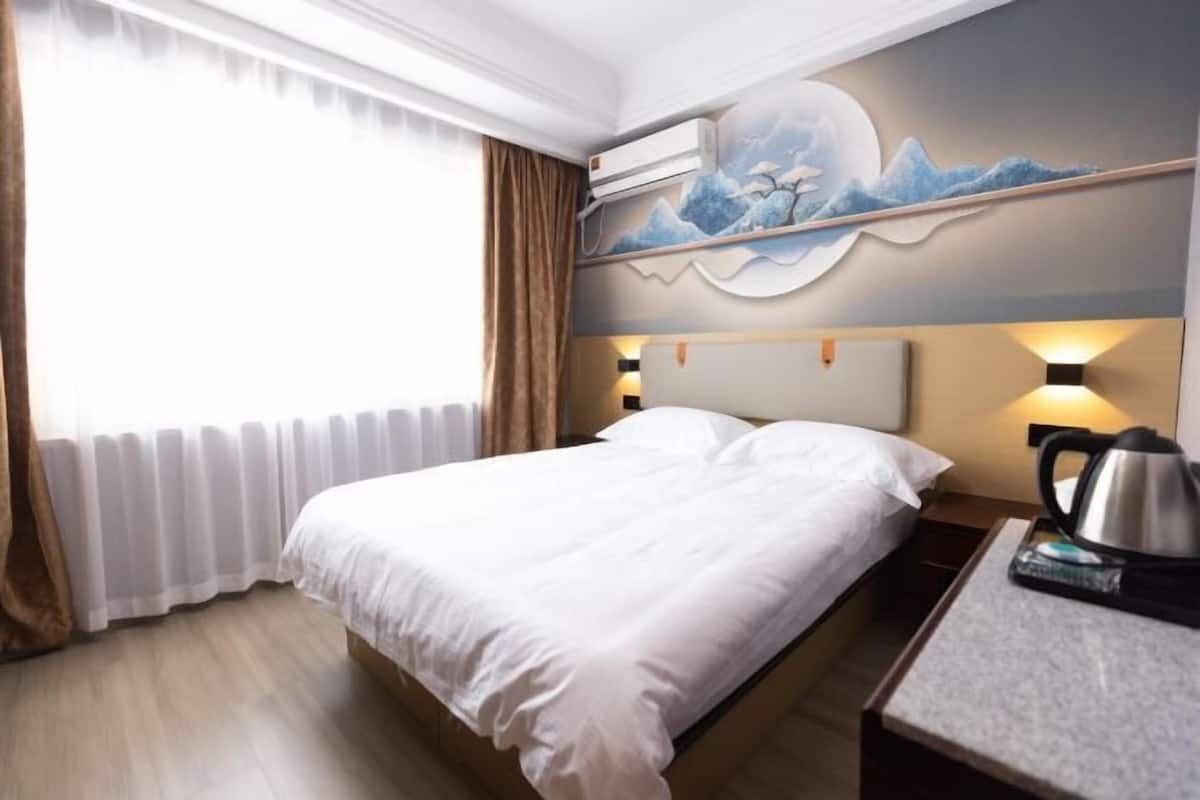 Une chambre d’hôtel équipée d’un lit, d’une table de chevet, d’une machine à café, d’un climatiseur mural et d’une fenêtre avec des rideaux.