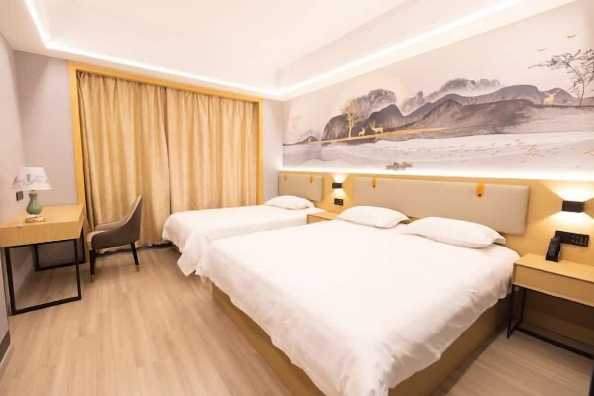 Une chambre d’hôtel avec deux lits, un bureau, une chaise, un tableau au mur et un rideau.