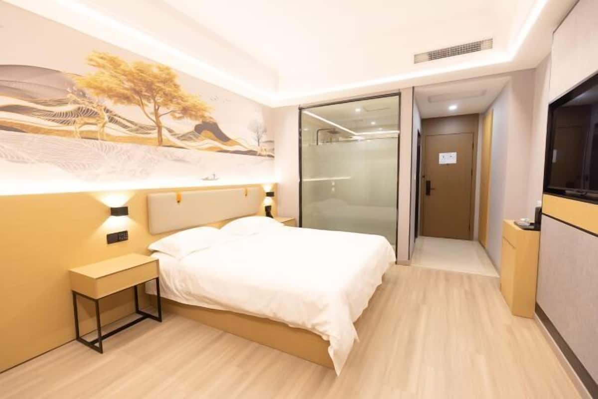 Une chambre d’hôtel moderne, équipée d’un lit, de tables de chevet, d’un tableau au mur, d’une porte coulissante et d’un téléviseur.