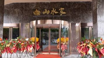Entrada de hotel con fachada curva, alfombra roja y arreglos florales.