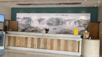 Un mostrador de recepción con un cuadro grande de una cascada y montañas, una pantalla de televisión y una pequeña mesa con una caja y una caja de pañuelos.