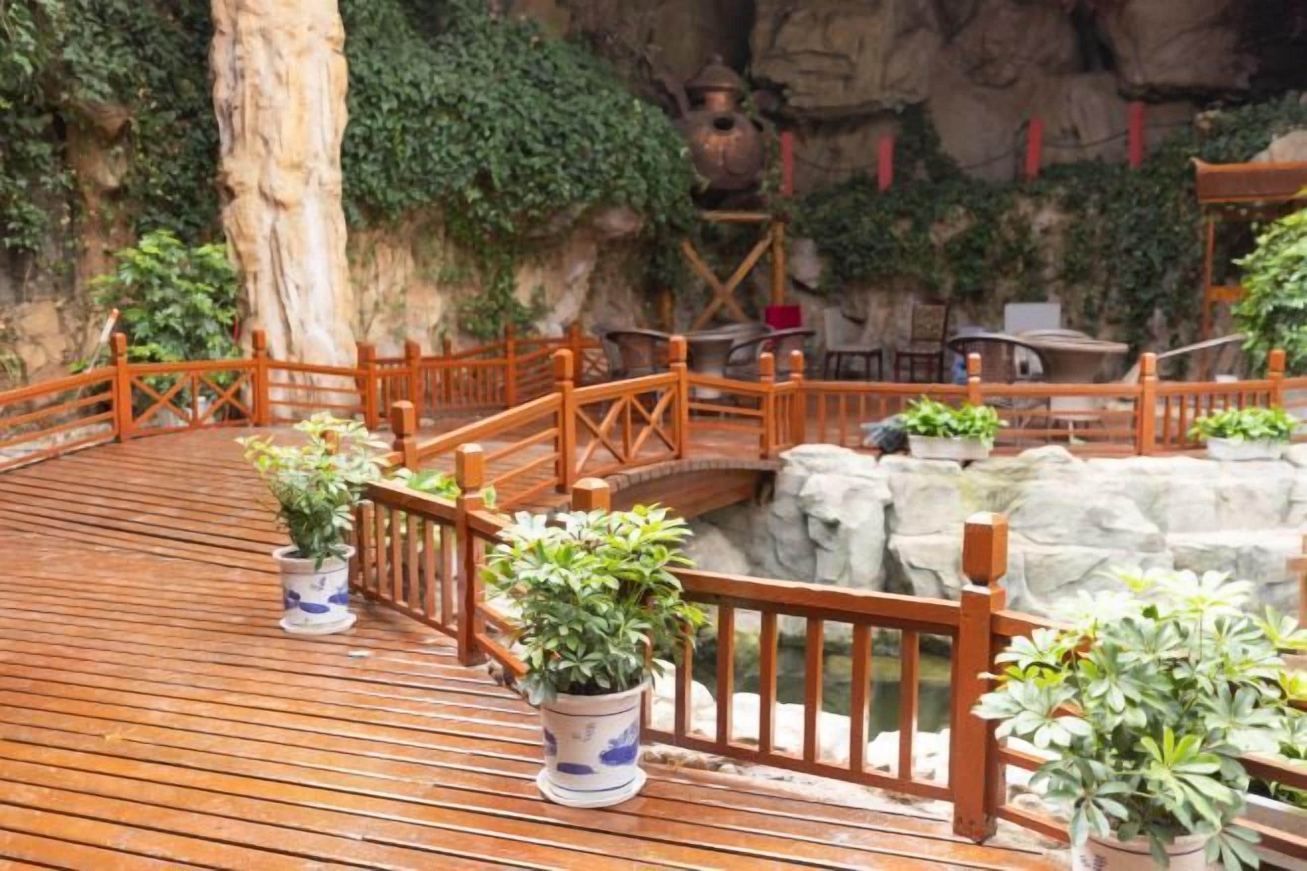 Une terrasse en bois agrémentée de plantes en pot, un pont en bois et un mur de pierres apparentes.