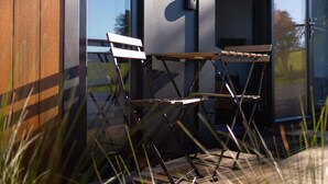 A folding table and chairs outside a building with a glass door and window, reflecting the surrounding environment. - Tussock Views by Tiny Away (Burkes Pass)