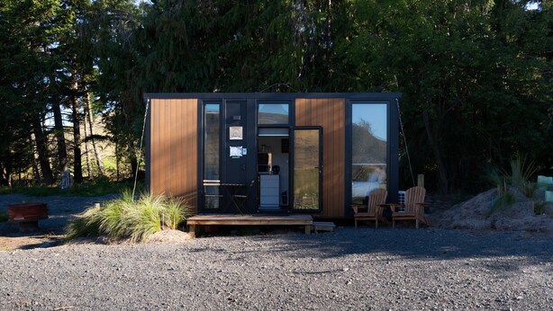 A modern cabin with a wooden exterior, a glass door, and a small outdoor seating area. - Tussock Views by Tiny Away (Burkes Pass)