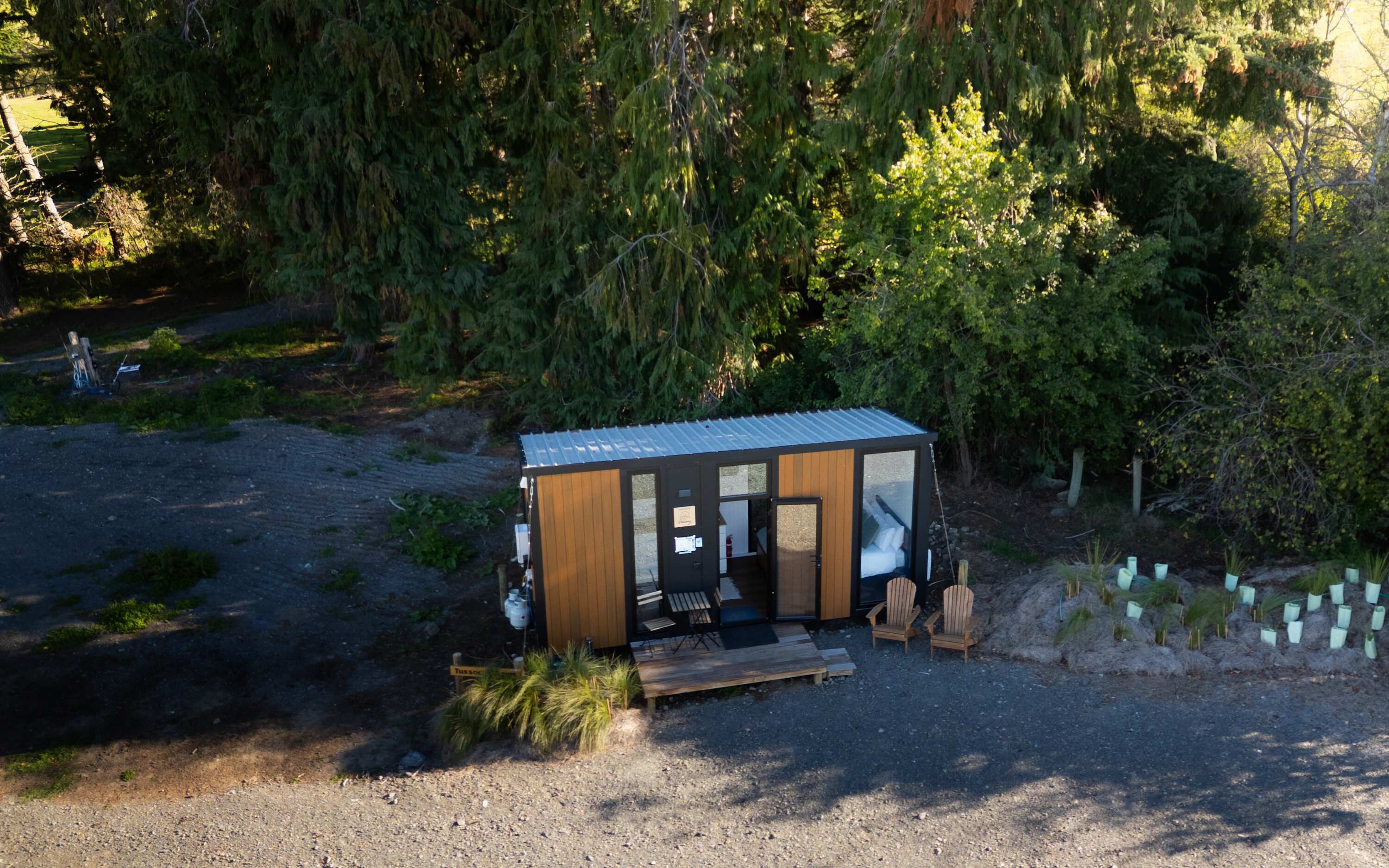 Eine kleine Holzhütte mit einem Metalldach, Holzwänden und einer Tür. Vor der Hütte stehen zwei Stühle und ein Tisch.