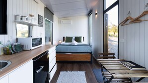A compact room with a bed, a small kitchenette, and a view through a large window. - Tussock Views by Tiny Away (Burkes Pass)
