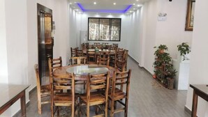 Un coin repas avec une table ronde et des chaises en bois, une plante en pot et une fenêtre donnant sur les arbres.