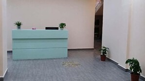 Un espace d’accueil avec un bureau bleu clair, deux plantes en pot et un escalier en arrière-plan.