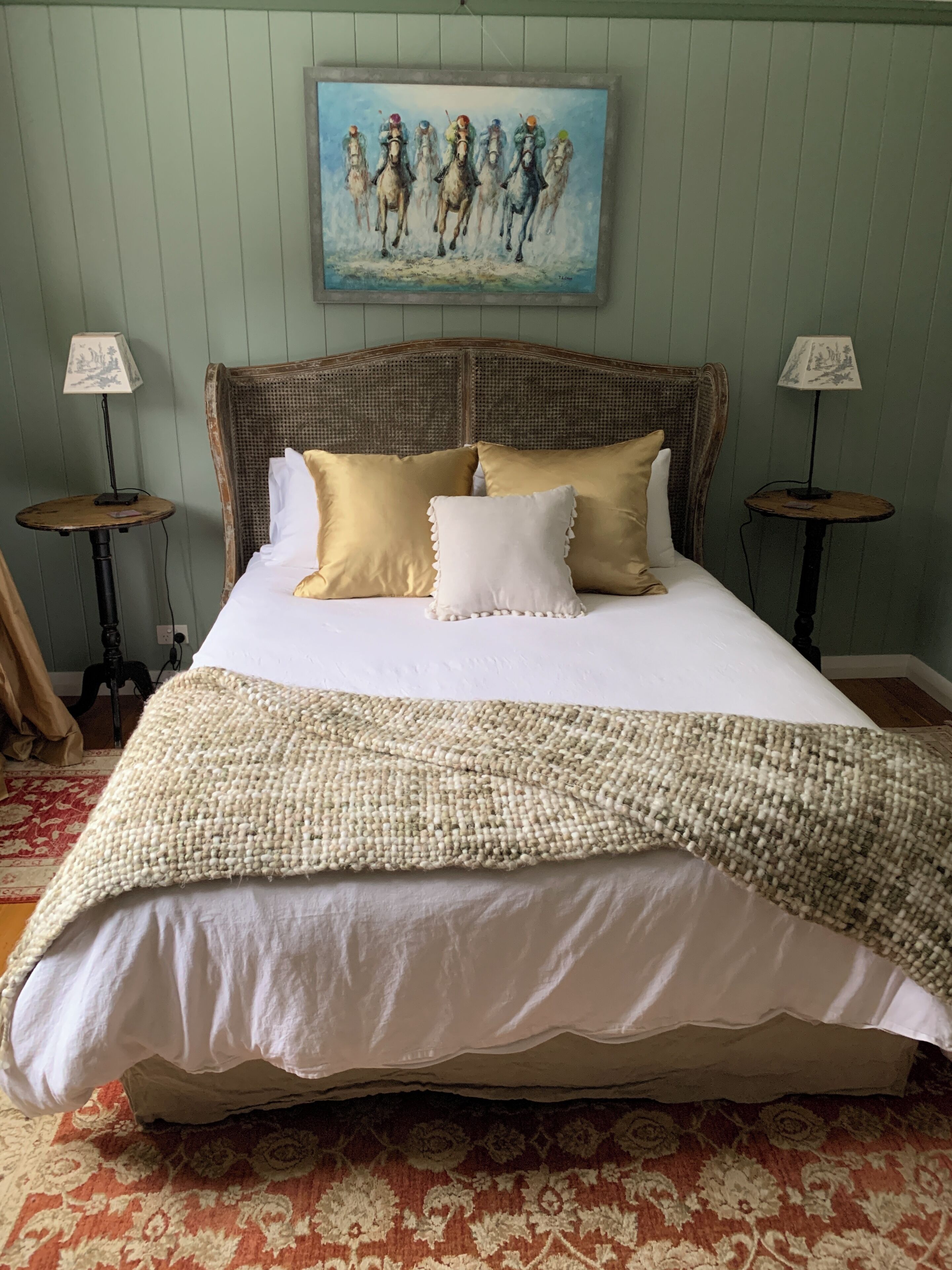 A bed with a woven blanket, two bedside tables, and a painting above.