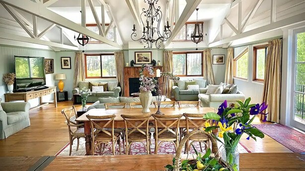 A spacious living room with a wooden dining table, multiple seating options, and large windows offering a view of the outdoors. - The Grange Berrima - The Ultimate Rural Retreat. Sleeps up to 13. (Berrima)