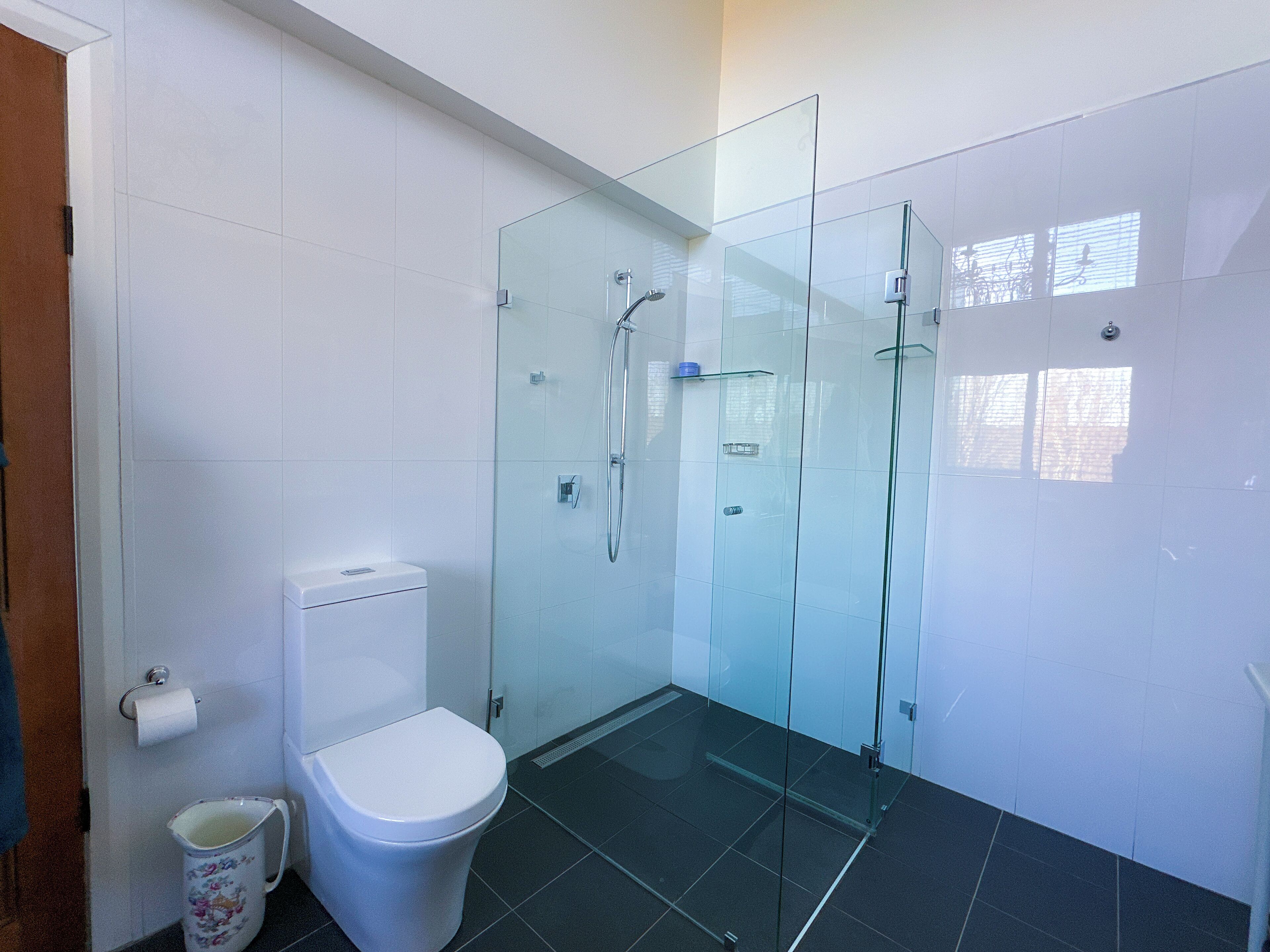 A modern bathroom with a glass-enclosed shower, a toilet, and a small trash bin.